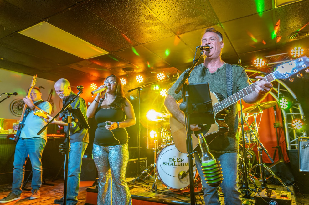 Photo of a Deep Shallow Band performance with Rusty Stevens playing guitar and singing, Jackie Fallar singing, Chip Cooper playing guitar and Rob Conrad playing bass.